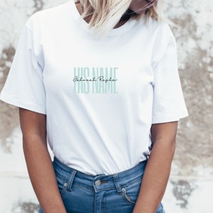 May include: A white t-shirt with the text "HIS NAME Jehovah Rapha HIS NAME" in a light teal color. The text is stacked vertically. The shirt is being worn with blue jeans.