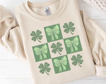 Peut inclure: Un sweat-shirt beige avec un motif à carreaux verts représentant des trèfles à quatre feuilles et des nœuds.