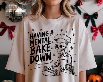 May include: White t-shirt featuring a black and white illustration of a skeleton baker rolling out dough. The text "Having a mental bake down" is printed on the shirt.