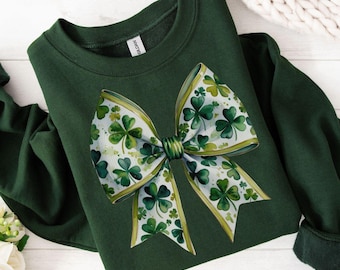 May include: A dark green sweatshirt with a white and green shamrock bow design. The bow is made of ribbon with shamrocks printed on it.