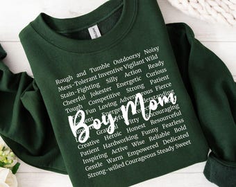 May include: A dark green sweatshirt with white text that reads "Boy Mom" surrounded by a list of positive adjectives describing a boy's personality.