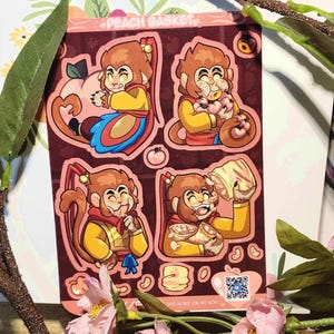 May include: Four sticker designs featuring a cartoon monkey in different poses. The monkey is wearing a yellow and red outfit and holding a peach, a pastry, or a bunch of peaches. The stickers are on a peach background with the text "Peach Basket" at the top.