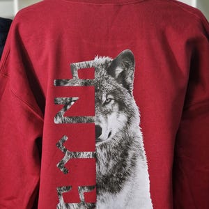 Op de afbeelding: Rood longsleeve sweatshirt met een wolf-print en het woord "FURY" gedrukt op de rug.
