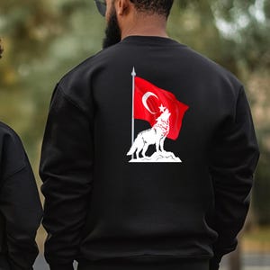 Op de afbeelding: Zwart sweatshirt met een witte wolf die huilt voor een rode Turkse vlag met een witte ster en halve maan.