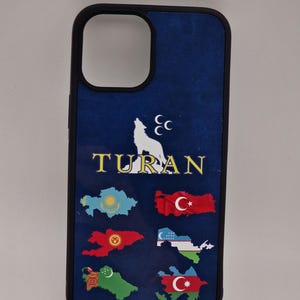 Op de afbeelding: Zwarte telefoonhoes met een donkerblauwe achtergrond. Het heeft een wit wolfsilhouet, halve manen en het woord "TURAN" in goud. De hoes toont ook kleurrijke kaartomtrekken met vlaggen.