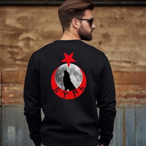 Op de afbeelding: Zwart sweatshirt met een rood halve maan- en sterontwerp. Een wolf die naar de maan huilt, bevindt zich in het midden van het ontwerp. De woorden "F.Y.N.H." staan in witte letters rond de maan.