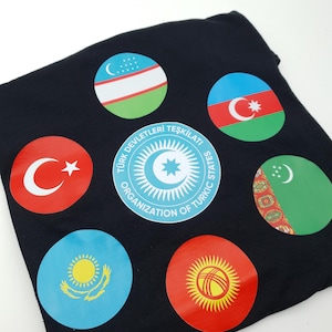 Op de afbeelding: Een zwart T-shirt met ronde patches van de vlaggen van Turkije, Oezbekistan, Azerbeidzjan, Kazachstan, Kirgizië en Turkmenistan. De middelste patch toont het logo van de Organisatie van Turkse Staten, dat in het Turks "Turk Devletleri Teskilati" en in het Engels "Organisation of Turkic States" luidt.