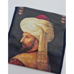 Op de afbeelding: Een schilderij van een man die een witte tulband draagt met een rode dop erop. Hij heeft een baard en kijkt naar links. De achtergrond is donker en er zijn drie gouden kronen in de rechterbovenhoek.