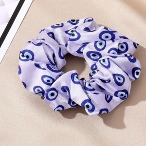 Könnte beinhalten: Lilafarbener Haargummi mit weißem Hintergrund und einem Muster aus blauen bösen Augen.