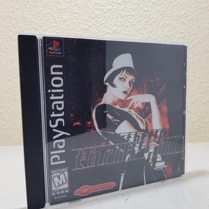 Op de afbeelding: PlayStation-spelcase met een rode en zwarte achtergrond. De titel van het spel is "Thrill Kill" en toont een vrouw in een zwarte jurk en een witte hoed. De PEGI-classificatie is "M" voor volwassenen.