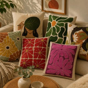 Puede incluir: Una colección de seis cojines cuadrados con diversos diseños, incluyendo una persona sosteniendo una hoja verde grande, un patrón floral abstracto verde y blanco, un estampado floral de cuadrícula roja y blanca y una ilustración de flor rosa brillante.