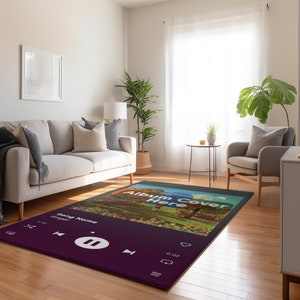 May include: A rectangular rug featuring a music player interface design. The rug is mainly dark purple with white icons and text, including "Album Cover Here" and "Song Name". The background image depicts a landscape.