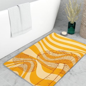 Può includere: Un tappetino da bagno giallo e bianco con un motivo a strisce ondulate e due illustrazioni di funghi marroni.