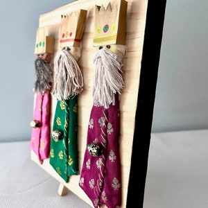 May include: Three wooden figures of the three wise men, each wearing a crown and a robe. The figures are standing on a wooden base with a black frame.