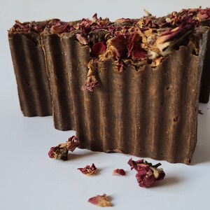 May include: Two brown bars of soap with dried rose petals on top. The soap is textured and has a rustic look.