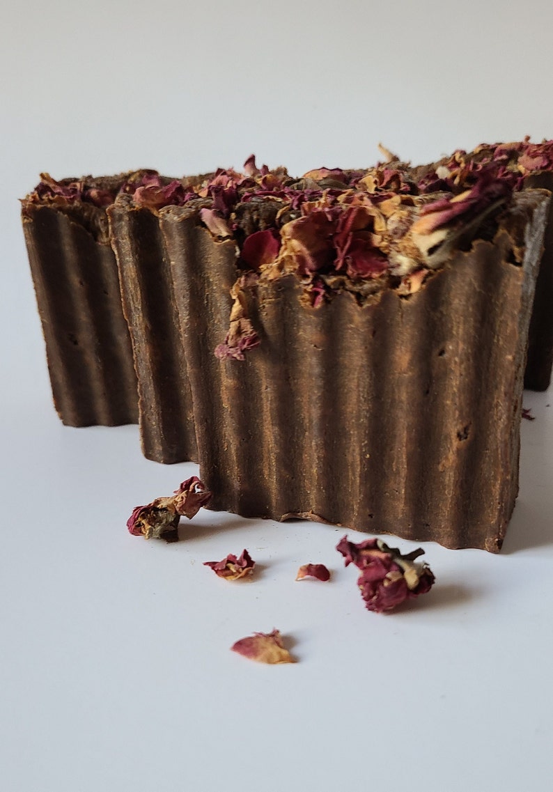 May include: Two brown bars of soap with dried rose petals on top. The soap is textured and has a rustic look.