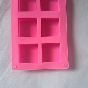 May include: Pink silicone mold with six square cavities. The mold is designed for making small soap bars or other crafts.