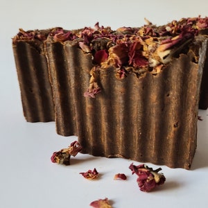 May include: Three brown bars of soap with dried rose petals on top. The soap is in a ribbed design.