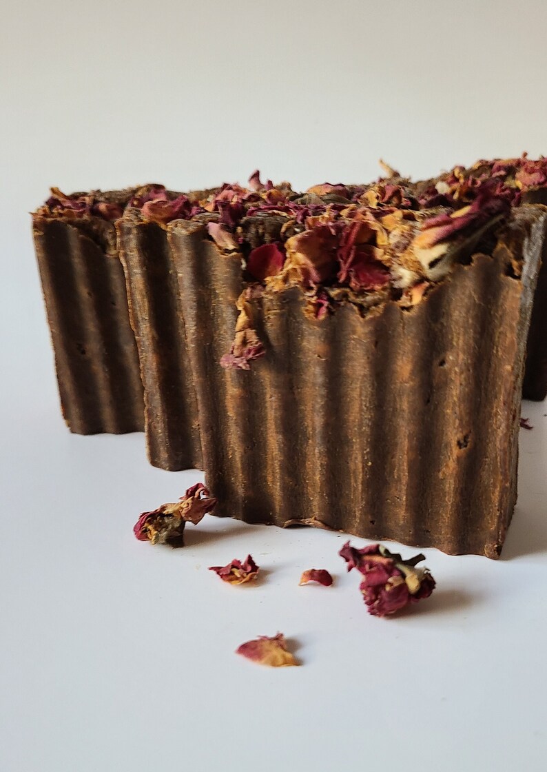 May include: Three brown bars of soap with dried rose petals on top. The soap is in a ribbed design.