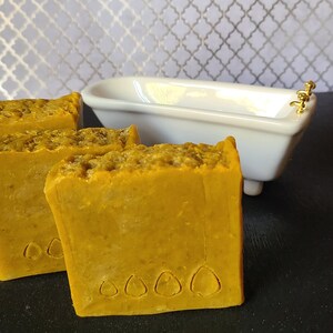 Può includere: Due saponette gialle con un motivo decorativo sul fondo. Il sapone è posto accanto a una vasca da bagno in porcellana bianca con accenti dorati.