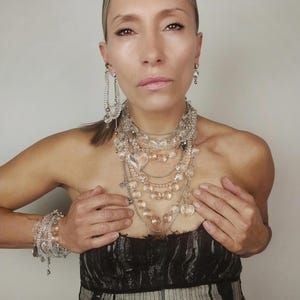 Clear quartz jewelry set including multi-row necklace, bracelets, and earrings for a complete statement look.
​Clear quartz statement jewelry set full look on a model featuring all layered pieces and crystal heart accents.