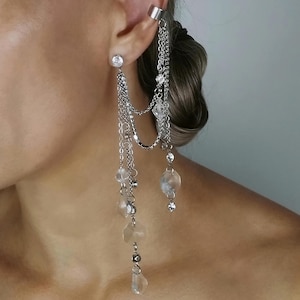 May include: Silver ear cuff and earring set. The ear cuff wraps around the upper ear, connected by chains to a stud earring and dangling chains with clear beads and crystals. A glamorous accessory.