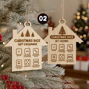 May include: Two wooden Christmas dice game ornaments shaped like houses. Each ornament has the text "Christmas Dice Gift Exchange" and dice instructions. The ornaments are hanging from twine and are decorated with Christmas trees.