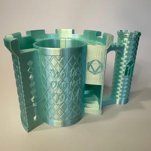 May include: A light green 3D printed castle-shaped mug with a tower on the side. The mug has a diamond pattern and the words "World's Okayest DM" are printed on the side.