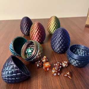 May include: A set of six iridescent dragon egg-shaped dice containers, with one open to reveal a set of six iridescent dice. The dice are a mix of d4, d6, d8, d10, d12, and d20.