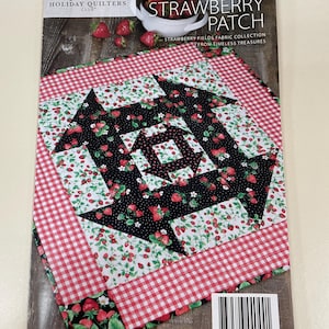 May include: A quilt pattern titled "Strawberry Patch" by Annie's Holiday Quilters Club. The pattern features a central design of black fabric with red strawberries, surrounded by white fabric with strawberries and a red and white gingham border.