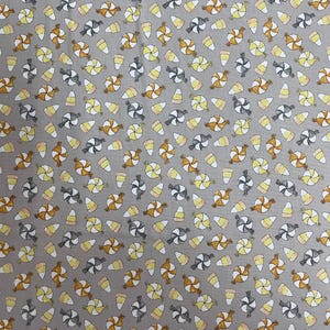 May include: Gray fabric with a repeating pattern of candies and candy corn. The candies are in orange, gray, and white, while the candy corn is yellow, orange, and white. This fabric is suitable for various craft projects.