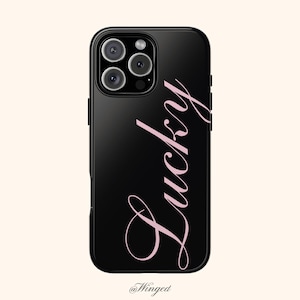 May include: A black smartphone case featuring a triple-lens camera module in the upper left corner. The word Lucky is printed vertically in a light pink cursive script font along the right side of the case. The text Winged is at the bottom.