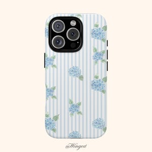May include: A white phone case with a blue and white striped pattern and watercolor-style blue hydrangea flowers. The case has a camera cutout and black side buttons. The @Winged logo is at the bottom.
