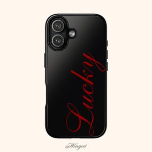 May include: Black phone case with a glossy finish. The word "Lucky" is written in red script on the back. The case has a dual-lens camera cutout and the @Winged logo at the bottom.