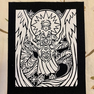 May include: Black and white embroidered patch featuring a stylised angel with wings, a halo, and a starburst behind the head. The angel is holding a shield with a face on it.