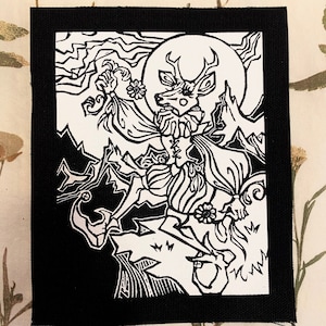 May include: Black and white patch with a detailed illustration of a deer with large antlers, a full moon, and a figure with flowing hair. The design is surrounded by mountains and floral elements. The patch has a black border.