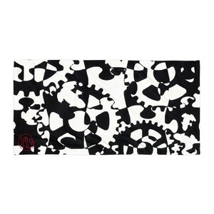 May include: A rectangular beach towel featuring a high-contrast black and white pattern of interlocking mechanical gears and cogs. A small, circular red logo with the letters MW is positioned in the lower left corner of the fabric surface.