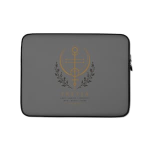 Op de afbeelding: Een antracietgrijze laptophoes met een goud en zwart grafisch ontwerp. In het midden staat een goud geometrisch symbool geflankeerd door zwarte bladtakken. Onderaan staat de tekst FREYIA, LOVE, BEAUTY, FERTILITY, WAR, MAGIC, SEIDR.