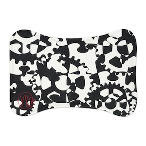 May include: A rectangular pet mat with rounded corners featuring a high-contrast black and white pattern of interlocking mechanical gears. A small red circular logo with the letters MW is printed in the bottom left corner of the mat.