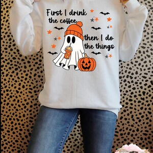 Könnte beinhalten: Weißer Pullover mit einem Geist, der einen Hut trägt und eine Kaffeetasse hält. Der Text auf dem Pullover lautet "First I drink the coffee then I do the things".