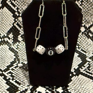 May include: A silver chain necklace with three black and white dice charms, including a black eight ball charm.