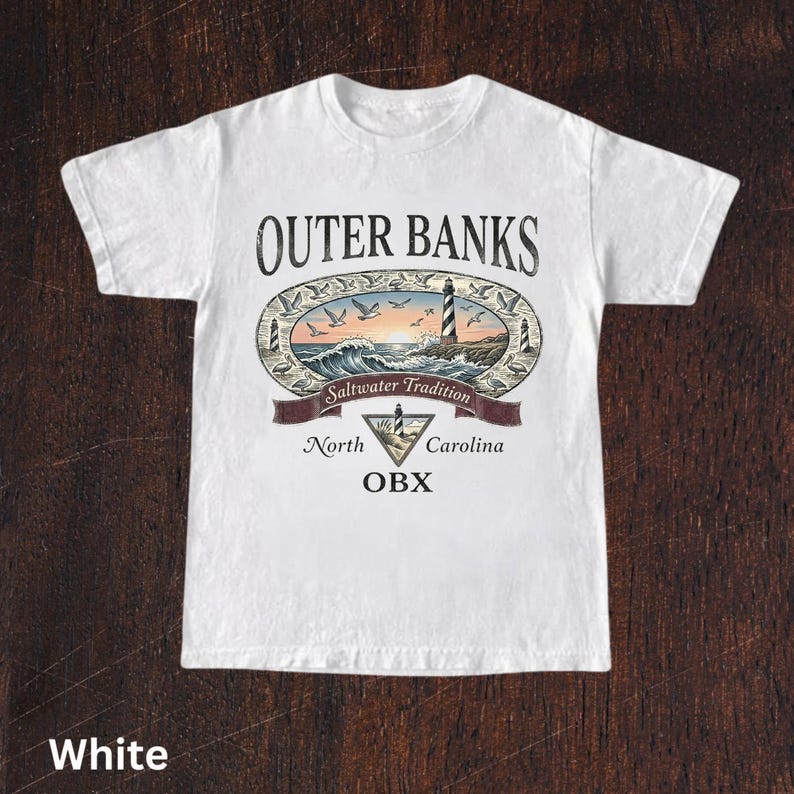 Puede incluir: Camiseta blanca con un dise&ntilde;o gr&aacute;fico colorido. El dise&ntilde;o incluye las palabras "Outer Banks" y "Saltwater Tradition", un faro, olas y p&aacute;jaros. Tambi&eacute;n est&aacute; presente el texto "North Carolina OBX".