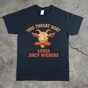 May include: Black t-shirt featuring a cartoon goat wearing a hot dog. The text on the shirt reads "This Throat Goat Loves Juicy Wieners".