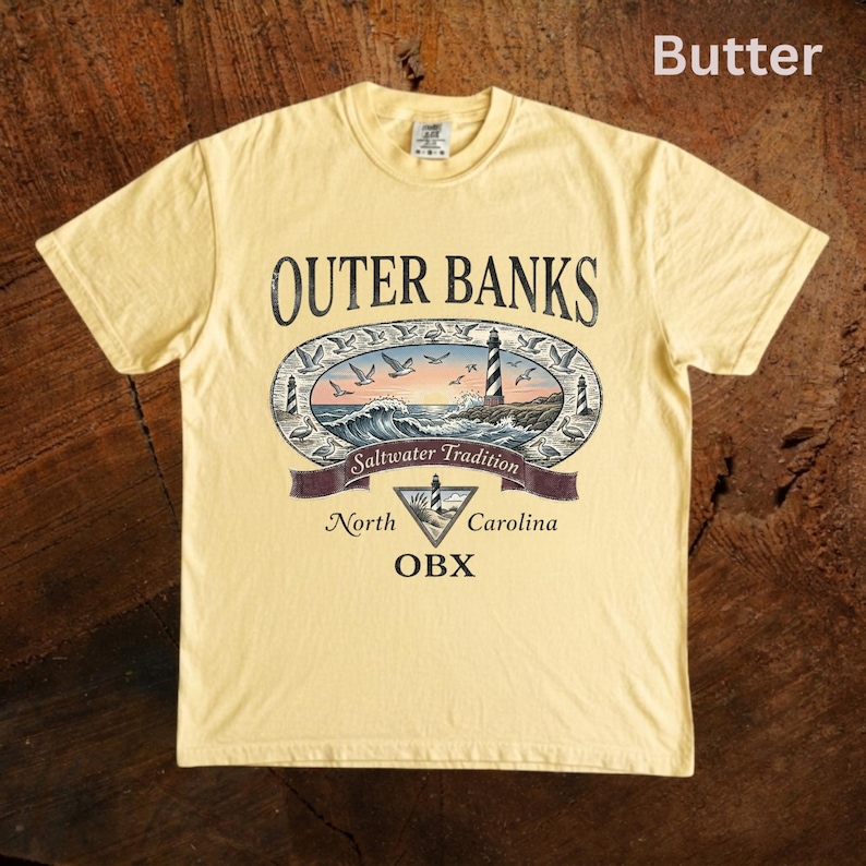 Puede incluir: Camiseta amarilla mantequilla con un dise&ntilde;o de Outer Banks. El gr&aacute;fico incluye un faro, olas y el texto "Saltwater Tradition, North Carolina, OBX". La camiseta est&aacute; hecha de un material suave.