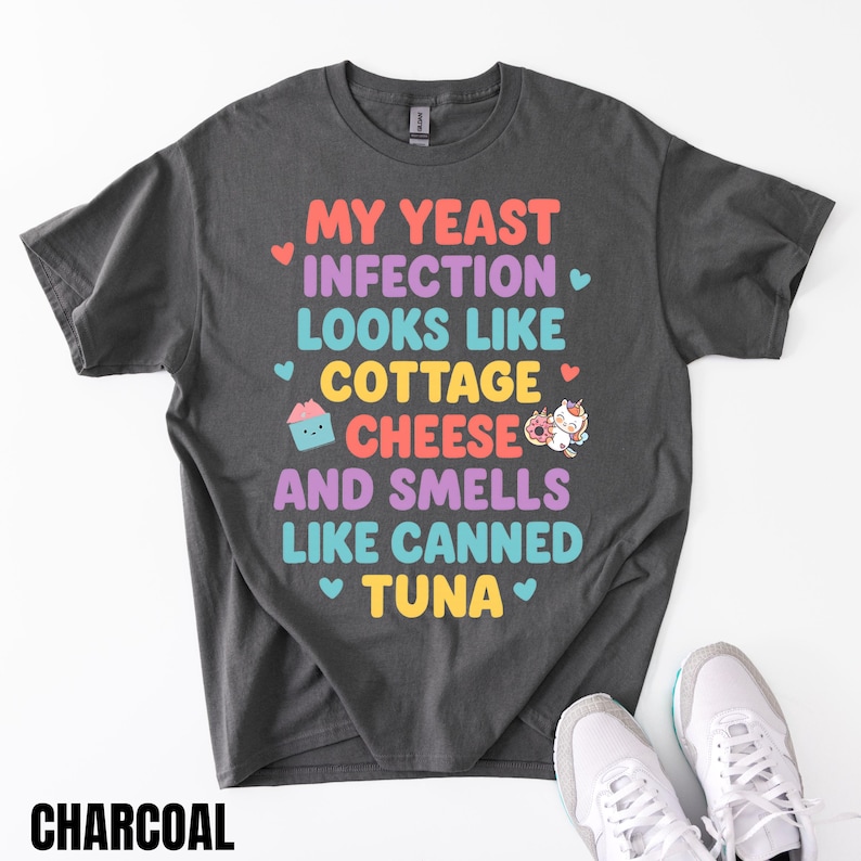 Puede incluir: Camiseta de color carb&oacute;n con el texto "MY YEAST INFECTION LOOKS LIKE COTTAGE CHEESE AND SMELLS LIKE CANNED TUNA". El texto est&aacute; en varios colores y fuentes. Una magdalena y un unicornio tambi&eacute;n aparecen en la camiseta.