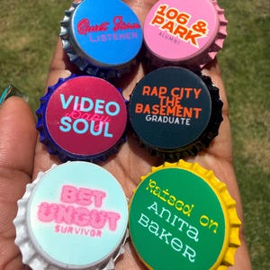 May include: Six circular bottle cap magnets featuring various text designs: blue with Quiet Storm Listener, pink with 106 & Park Alumni, dark pink with Video Soul, black with Rap City The Basement Graduate, light blue with BET Uncut Survivor, and green with Raised on Anita Baker.