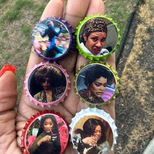 May include: A collection of six bottle caps with images of various people. The caps have colorful edges, including purple, green, pink, red, and white. The images on the caps feature different individuals, each with unique expressions and styles.