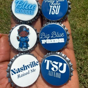 May include: Six circular bottle cap pins featuring blue and white designs. Text includes Blue Blooded, Pretty Girls Choose TSU, Big Blue Pride, Nashville Raised Me, and TSU Alumni. One pin features a cartoon character wearing a blue outfit.