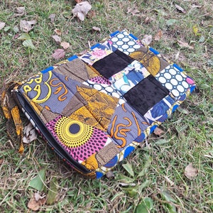 May include: A colorful patchwork fabric clutch bag with a black zipper and a black strap. The bag is made of different fabrics with geometric and floral patterns in shades of blue, yellow, pink, and black.