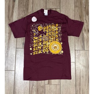 Könnte beinhalten: Burgunderfarbenes T-Shirt mit gelbem Grafikdesign mit den Worten "Devils" und "Sun Devils". Das Design beinhaltet ein Teufelsmaskottchen und "Arizona State University 1885".